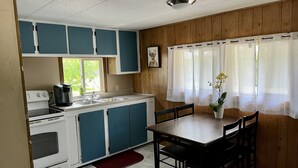 Una cocina compacta con armarios blancos y azules, una estufa y un fregadero. Hay una mesa de comedor con sillas y una planta en maceta.