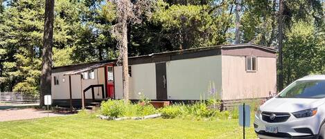 A mobile home with a red door, a covered porch, and a small window.