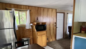 Cocina compacta con refrigerador, microondas, gabinetes de madera y una mesa de comedor.