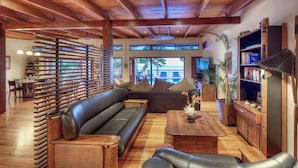 A spacious living area with a wooden ceiling, a black leather sofa, a wooden coffee table, and a bookshelf.