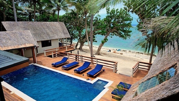 A pool area with lounge chairs, a hot tub, and a beach view.