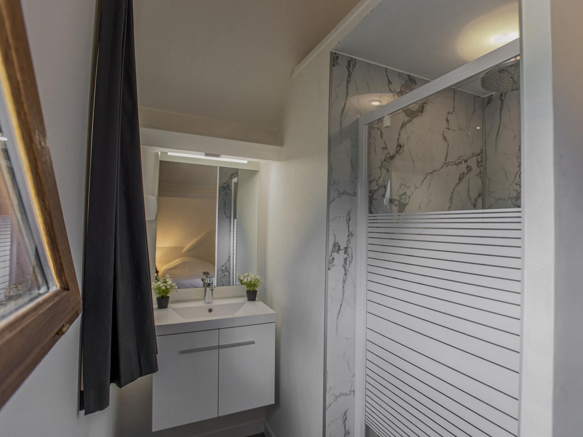 Ein Badezimmer mit weißem Waschtisch, einem Spiegel, einer Dusche mit Marmorwänden und einem gerahmten Bild an der Wand.