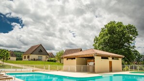 Una piscina con sillones de descanso, un pequeño pabellón y casas al fondo.