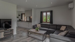 Una sala de estar moderna con sofá, mesa de centro, televisor y una cocina al fondo.