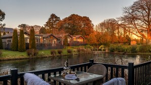 A riverside view with a dining area featuring wicker furniture and a table with a glass of wine. - Killington Lodge, Kentisbury Grange (Barnstaple)