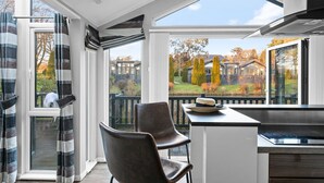 Ett modernt kök med ett stort fönster, en matplats med en stol och utsikt över ett bostadsområde.