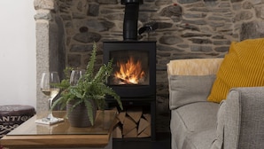 A cozy room with a stone wall, a fireplace, a sofa with a yellow cushion, and a table with a glass and a plant. - Eastleigh Cottage - sleeps 4 guests  in 2 bedrooms (Marazion)