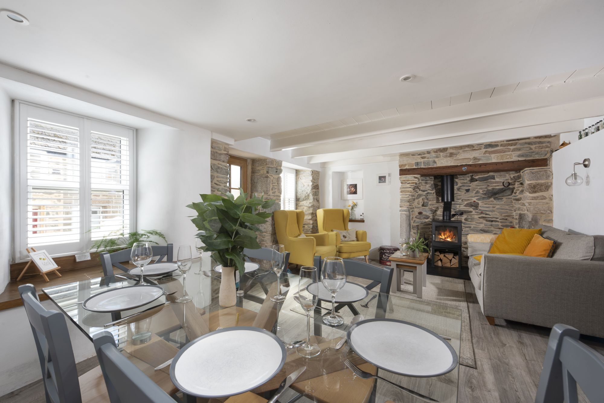 A modern living room with a glass dining table, yellow armchairs, and a stone fireplace.