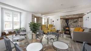 A modern living room with a glass dining table, yellow armchairs, and a stone fireplace. - Eastleigh Cottage - sleeps 4 guests  in 2 bedrooms (Marazion)