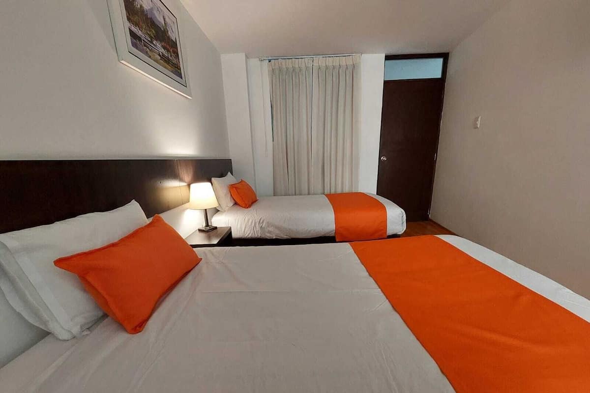 Une chambre d’hôtel avec deux lits, une table de chevet avec une lampe, une porte et une fenêtre avec des rideaux.