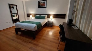 A hotel room with a wooden floor, a bed with green bedding, two bedside lamps, a desk, a chair, a mirror, and a framed picture on the wall. - Hotel Toulouse Arequipa (Arequipa)