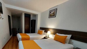 A hotel room with two beds, each with white bedding and orange accents, a bedside table with a lamp, and a framed picture on the wall. - Hotel Toulouse Arequipa (Arequipa)
