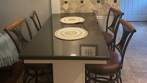 A dining area with a black table, four chairs, two placemats, a pendant light, a framed picture on the wall, and a tiled backsplash. - Home in Groves (Groves)