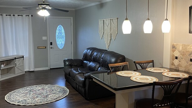 A spacious living area with a black leather sofa, a dining table with four chairs, and a ceiling fan. - Home in Groves (Groves)