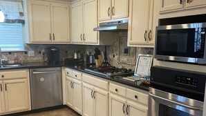 A kitchen with white cabinets, stainless steel appliances, and a tiled floor. - Home in Groves (Groves)