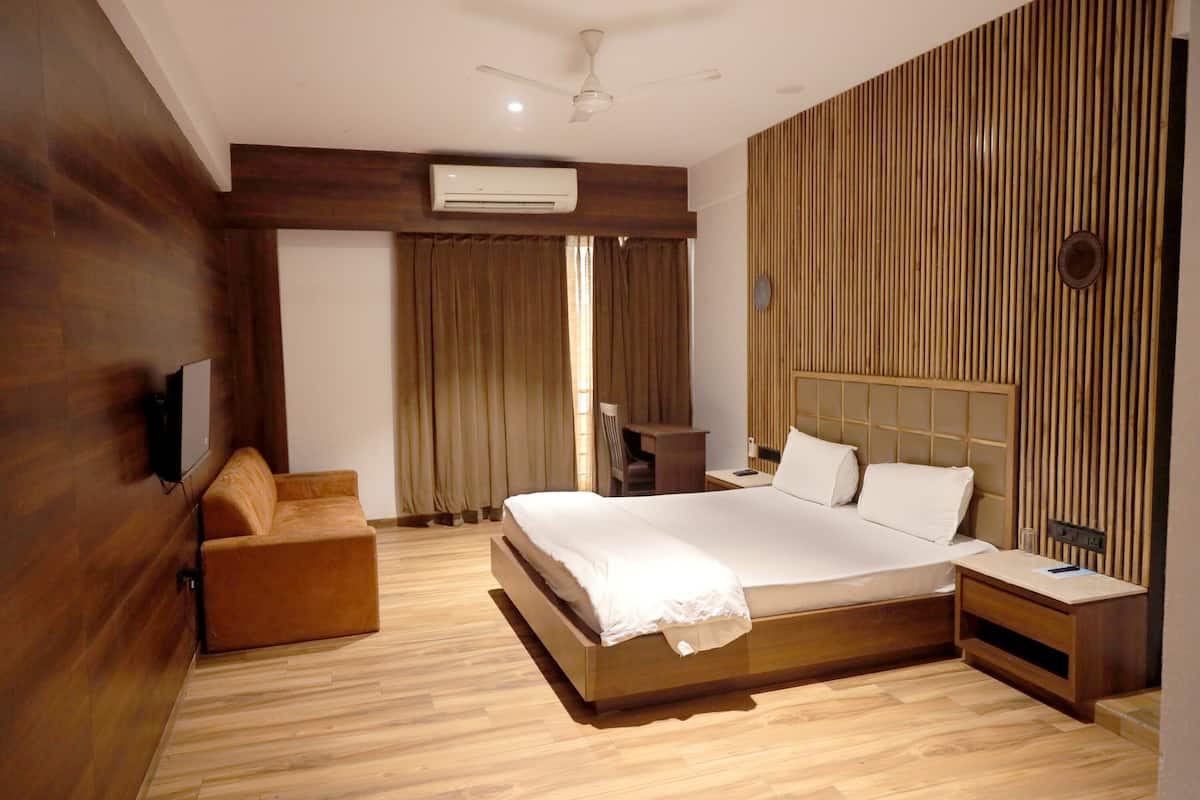 A modern hotel room with a wooden floor, a large bed, a wooden headboard, a small wooden nightstand, a wooden bench, and a ceiling fan.