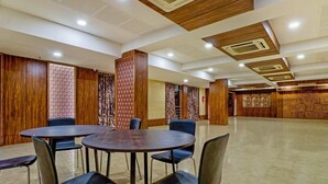 Una habitación amplia con una mesa redonda y sillas, paneles de madera y cortinas estampadas.