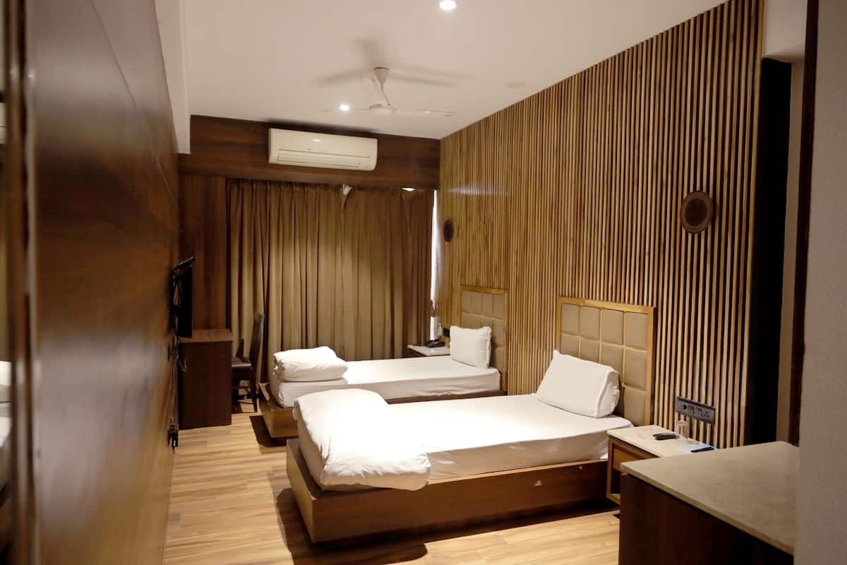 A hotel room with two beds, wooden flooring, a ceiling fan, an air conditioning unit, and a wooden panel wall.