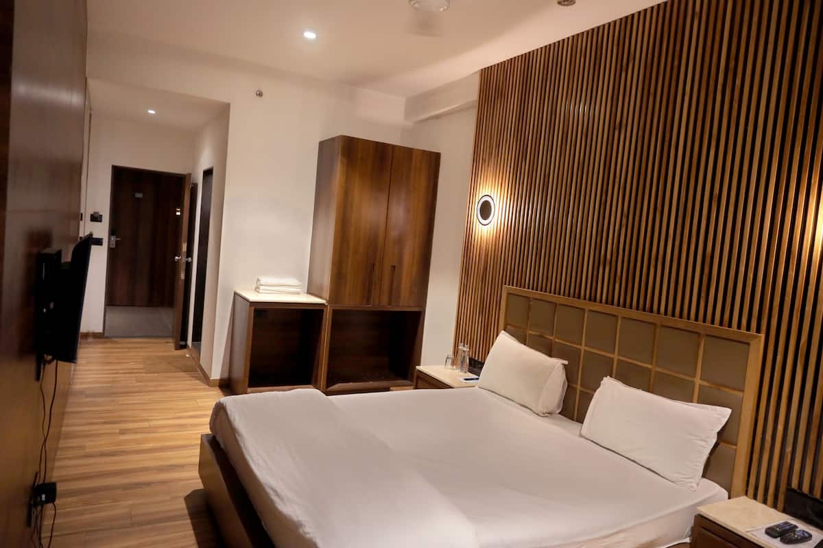 A modern hotel room with a large bed, wooden wardrobe, and a desk with a chair.