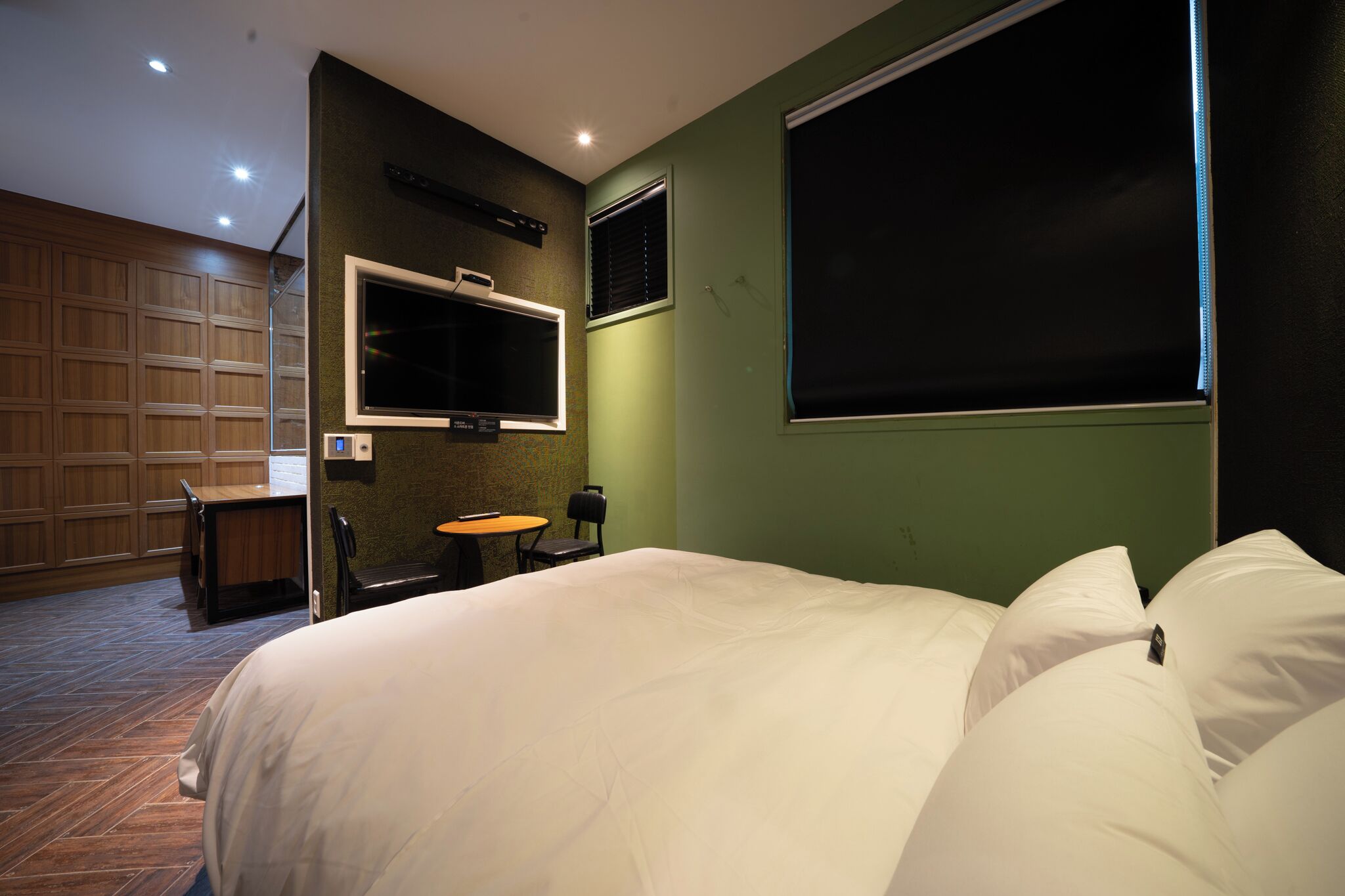 A hotel room with a large bed, a desk, a chair, a TV mounted on the wall, and a window.