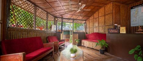 A wooden-floored room with a red sofa, a small table with a plant, and a ceiling fan.