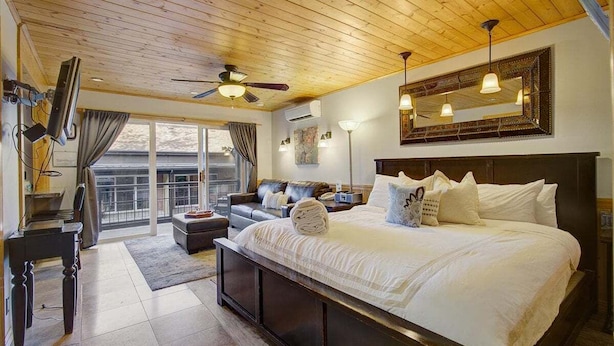 Un dormitorio con una cama grande, ventilador de techo, televisión y balcón con cortinas.