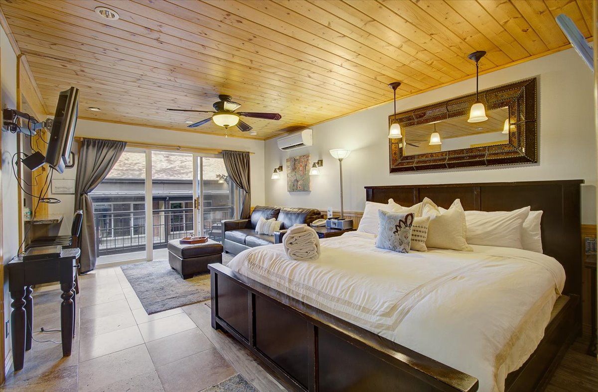 A bedroom with a large bed, a desk, a sofa, and a ceiling fan.