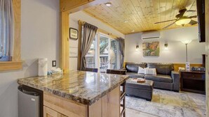 Cocina con encimera de granito, armarios de madera y lavavajillas integrado. Hay un comedor con mesa y sillas, y una sala de estar con sofá y mesa de centro.