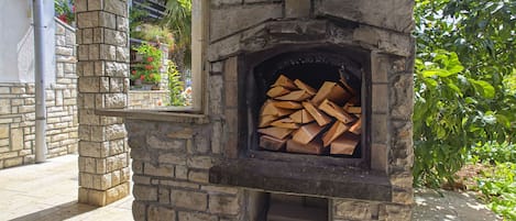 A stone-built outdoor fireplace with a firewood stack inside.