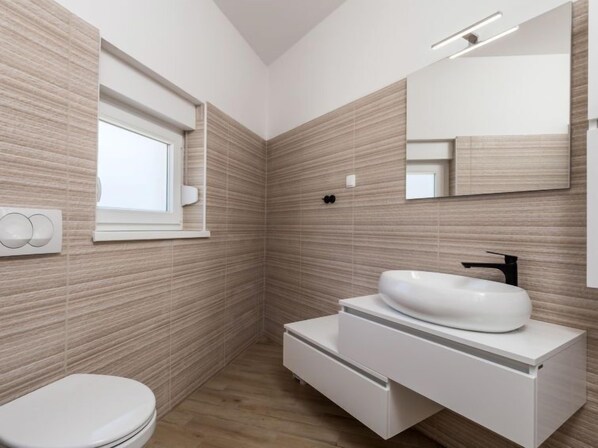 Une salle de bain moderne avec des toilettes blanches, un lavabo blanc dot é d’un robinet noir et un miroir au-dessus du lavabo.