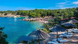 A beach with clear blue water, white lounge chairs, and thatched umbrellas. - Villa Palma by Interhome (Krk/Pinezići)