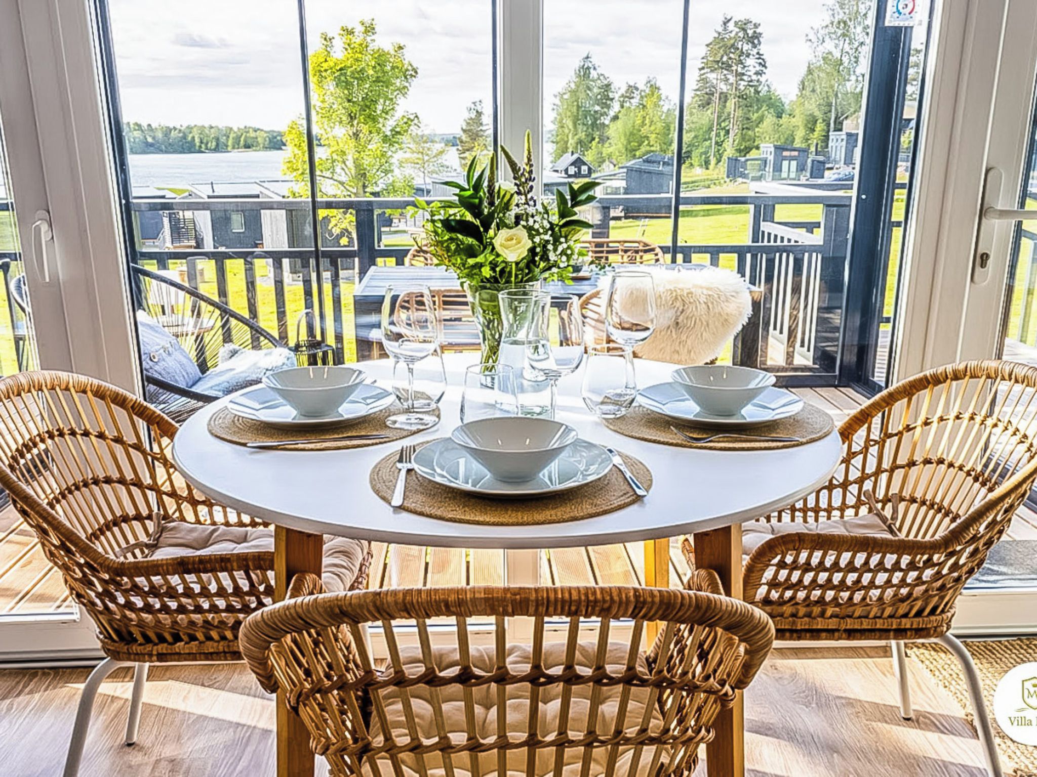 A round table with four chairs, a vase with flowers, and a view of a lake and buildings.