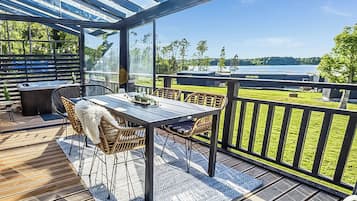 A covered outdoor area with a table and chairs, a view of a lake, and a wooden deck.