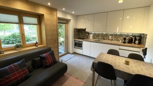 A modern kitchen with white cabinets, a dining table, and a sofa with plaid cushions. - Ilse EG Süd-West by Interhome (Fiesch)