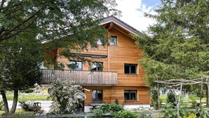 A two-story wooden house with a balcony, surrounded by a garden with various plants and a small greenhouse. - Ilse EG Süd-West by Interhome (Fiesch)