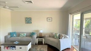 Ein Wohnzimmer mit zwei Sofas, einem Couchtisch und einer Lampe. Es gibt einen Deckenventilator und ein Fenster mit Blick ins Freie.