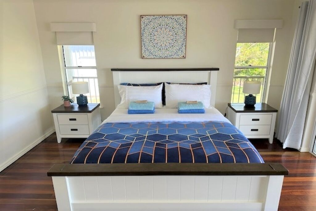 A bedroom with a large bed, two bedside tables, a wall-mounted artwork, and a window with curtains.