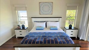 Ein Schlafzimmer mit einem großen Bett, zwei Nachttischen, einem Wandbild und einem Fenster mit Vorhängen.