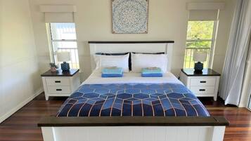 A bedroom with a large bed, two bedside tables, a wall-mounted artwork, and a window with curtains.
