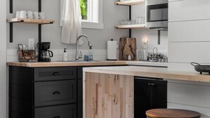 A modern kitchen with black cabinets, a wooden island, and a bar stool. - H Studio Close to Downtown Beaches Wineries (Traverse City)