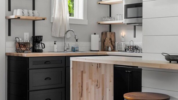 A modern kitchen with black cabinets, a wooden island, and a bar stool.