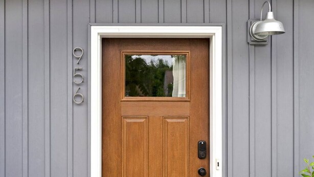 A wooden front door with a small window, a mailbox, and a wall-mounted light fixture.