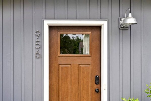 Une porte d’entrée en bois avec une petite fenêtre, une boîte aux lettres et un luminaire fixé au mur.