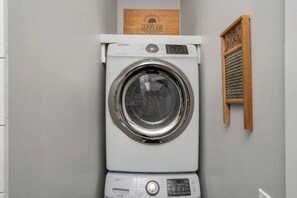 A front-loading Samsung washing machine in a laundry room with a wooden sign above it and a wooden hand dryer to the right. - H Studio Close to Downtown Beaches Wineries (Traverse City)