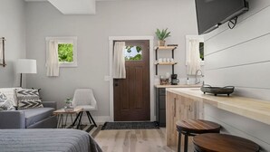 A compact, modern room with a bed, a small seating area, a kitchenette, and a TV mounted on the wall. - H Studio Close to Downtown Beaches Wineries (Traverse City)