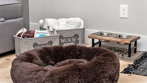 A pet-friendly room with a grey sofa, a pet bed, a pet food station, and storage bins labeled 'Fetch' and 'WOOF'. - H Studio Close to Downtown Beaches Wineries (Traverse City)