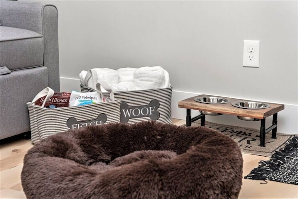 A pet-friendly room with a grey sofa, a pet bed, a pet food station, and storage bins labeled 'Fetch' and 'WOOF'. - H Studio Close to Downtown Beaches Wineries (Traverse City)