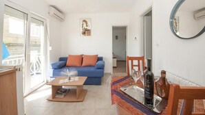 Una sala de estar con un sofá azul, una mesa de centro de madera y una zona de comedor con una mesa preparada para dos.