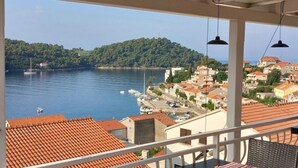 Un balcón con vistas a un pueblo costero, un puerto deportivo con barcos y edificios con tejados de teja.