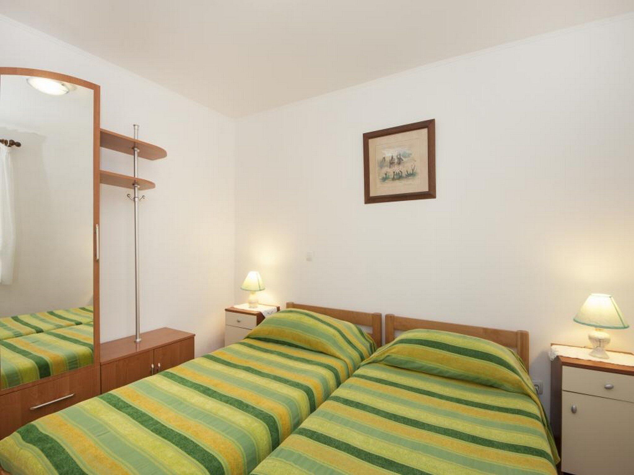 Ein Hotelzimmer mit zwei Betten, einem Holzschrank, einem Spiegel, einem gerahmten Bild an der Wand und Nachttischlampen.